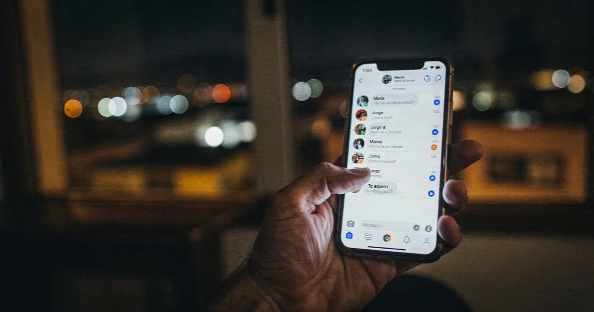 Mano sosteniendo un celular de noche con la bandeja de conversaciones abierta